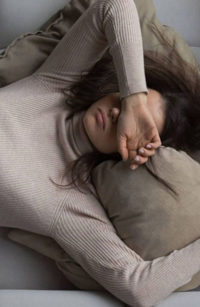 mulher deitada voltada para cima com os braços pousados ao lado da cabeça e uma mão a tapar os olhos