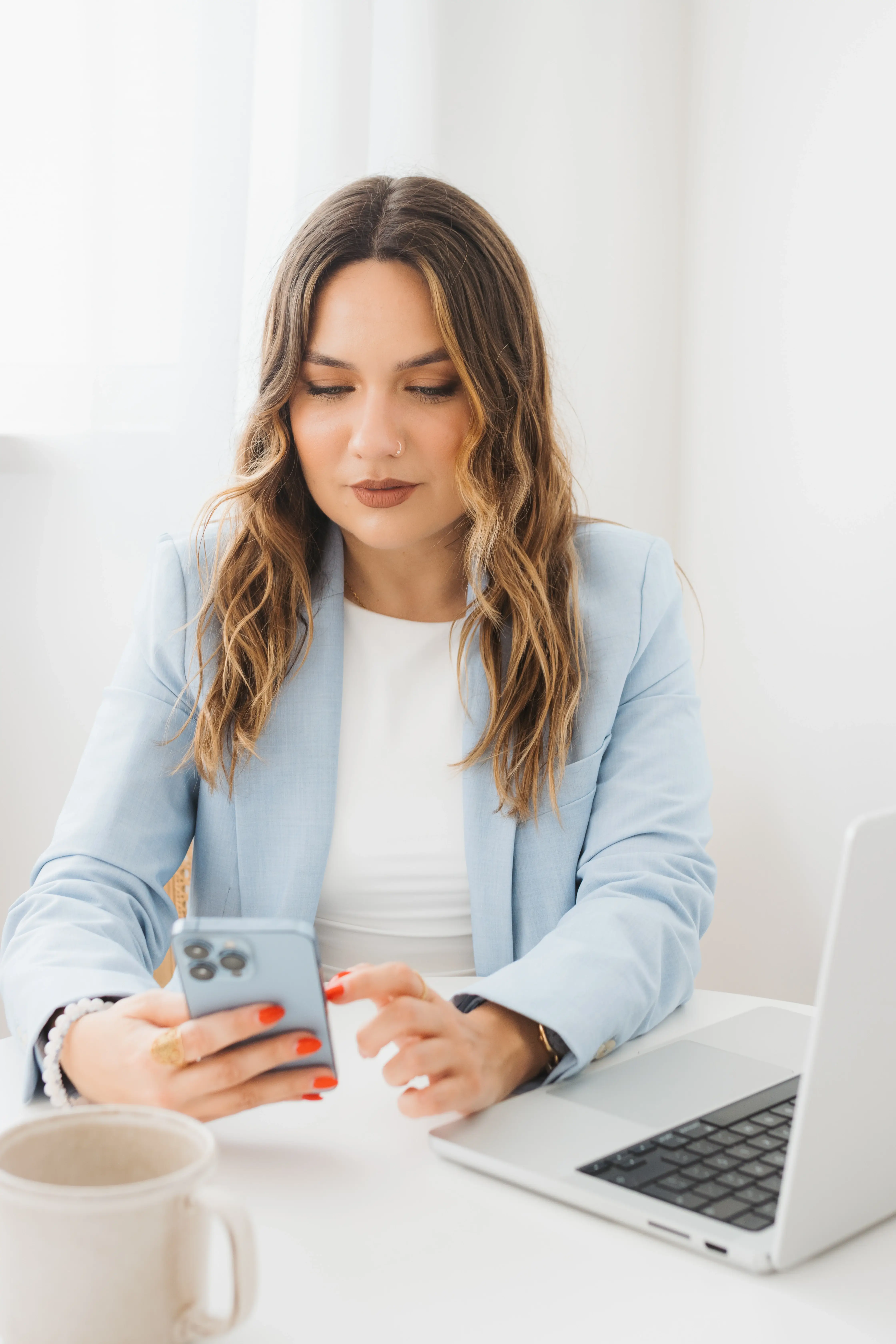 soraia, hipnoterapeuta, sentada à secretária concentrada a olhar para o telemóvel, com o computador ao lado. Focada.